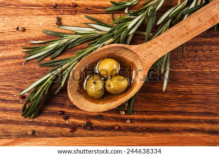 Olive oil and olives in wooden spoon with rosemary and spices, lying on the wooden table