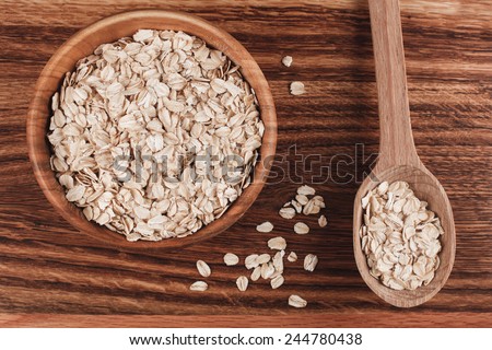 Wooden bowl of oat with wooden spoon on wooden table