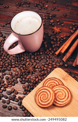 Cup of coffee with foam, cinnamon sticks, star anise, coffee beans and wooden board with round cookies, staying on the wooden table