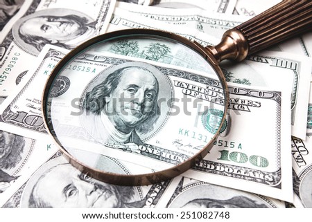 One hundred dollars banknotes lying on wooden table with vintage magnifying glass