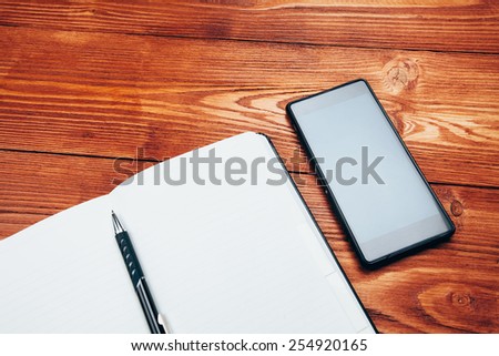 gadget mobile cell phone and notebook with pen on a wooden table