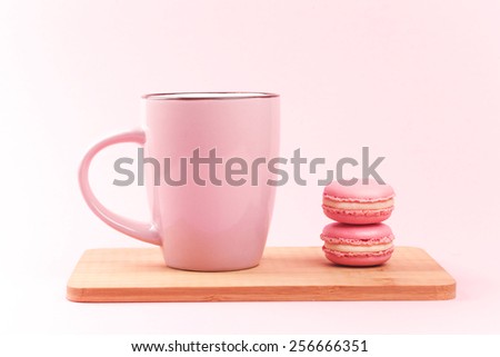Pink french macaroons and pink cup of coffee lying on wooden board, on pink background
