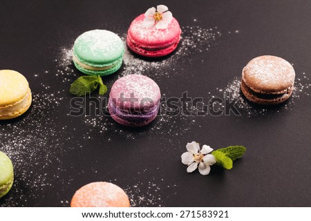 French colorful macaroon with powdered sugar, lying on black background
