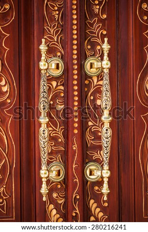 Golden vintage door handles on a wooden door with a carved pattern