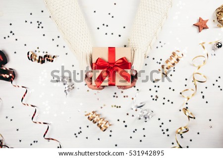 Female hands holding present with red bow on white rustic sparkling background. Festive backdrop for holidays: Birthday, Valentines day, Christmas, New Year. Flat lay