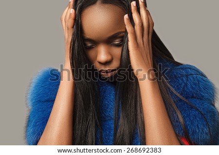Beautiful black girl in a blue coat and loose long black hair closes palms ears and looking down