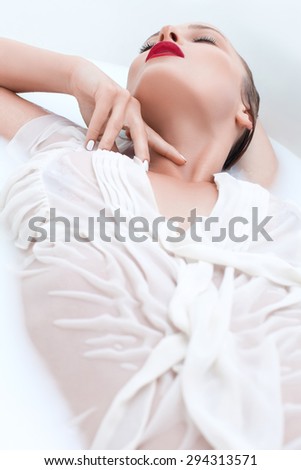 Beautiful young girl in a white blouse lying in the bathroom with white water, milk , passionately bent and touching the neck with his hand