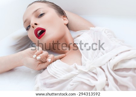 Beautiful young girl in a white blouse lying in the bathroom with white water, milk , passionately bent and touching the neck with his hand