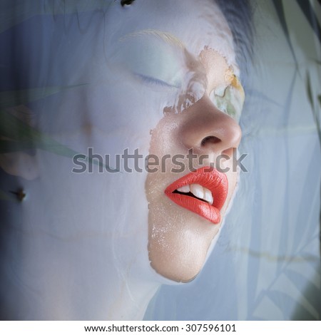 Portrait of a beautiful young girl sinks  wall of water. Bright orange lips fern leaves and mustard jacket. Closed eyes under water. Breathing. Harmony.