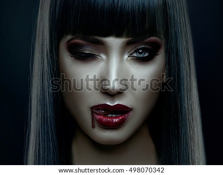 Portrait of vampire look of  woman for halloween,wearing long black hair, dark, bright make up,blinking and liking the blood drop in the corner of her mouth