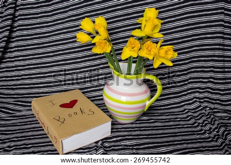 Daffodils in vase and book with cover I love books on striped background, shallow depth of field.