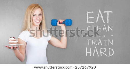 Beautiful young fitness model woman with a plate full of Sweets Cake Candy and dumbbell (weight) - Weight loss diet - Isolated on old grey wall background with EAT CLEAN AND TRAIN HARD text