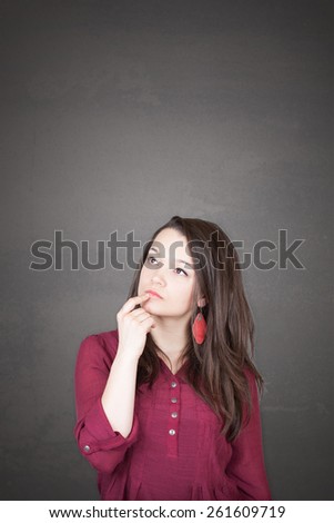 Beautiful young and pretty woman thinking (have no idea) in front of old grey wall background with place for your text design or drawing