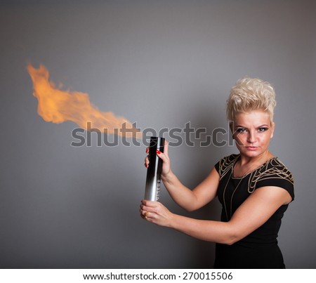 Very attractive and stylish professional hairdresser woman with flaming hair spray. With stylish blonde hair. In elegant outfit on grey background