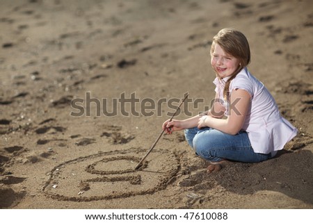 Happy blonde young girl on the beach writing the number ten in the sand, smiling, selective focus on writing