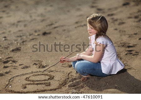 Blonde young girl on the beach writing the number ten in the sand, selective focus on writing