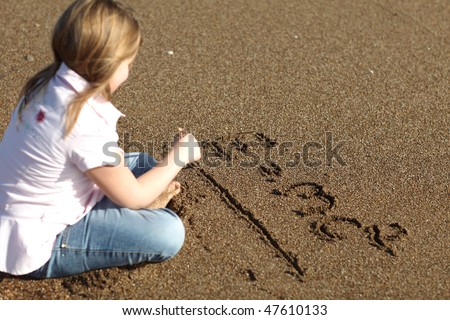 Blonde young girl writing mathematical formula in the sand, shallow depth of field, selective focus on writing
