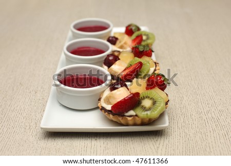 Beautiful decorated fruit tarts with strawberry sauce; shallow depth of field