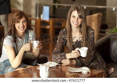 Two beautiful young women with great teeth enjoying their lunch break, drinking coffee, smiling to the camera