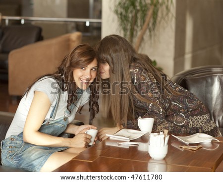 Two beautiful young women enjoying their lunch break, drinking coffee, sharing a secret.