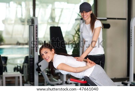 Two happy young women in the gym smiling to the camera, pool in the background
