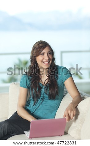 Happy young woman with laptop smiling to the camera, palm tree, sea and mountains in the background.