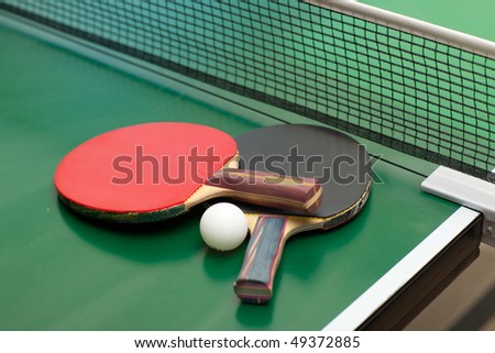 Two table tennis or ping pong rackets and ball on a green table with net; shallow DOF, focus on rackets