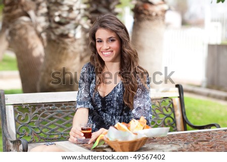 Beautiful young woman with great smile enjoying her breakfast outside, drinking tea, smiling to the camera; shallow depth of field