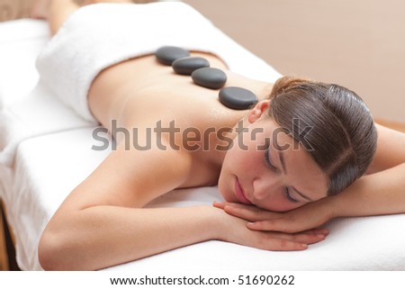 Beautiful young woman enjoying a hot mineral stone treatment in spa, shallow depth of field, focus on face