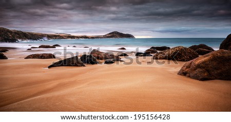 Coastal sunset with soft waves washing over the beach and rocks