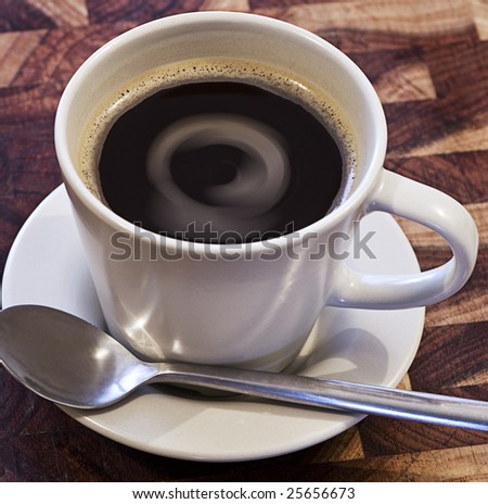 A cup of coffee sitting on a saucer with interesting swirls in liquid.