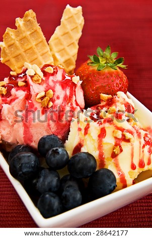 An ice cream sundae in a bowl. Made with vanilla and strawberry ice cream, blueberries, strawberries, waffles and strawberry topping.