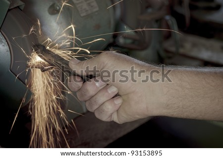 Male hand holding a metal rod amongst sparks on a bench grinder.