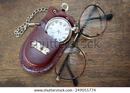 Vintage metallic glasses frame with pocket watch on the wooden table. Reading accessories.
