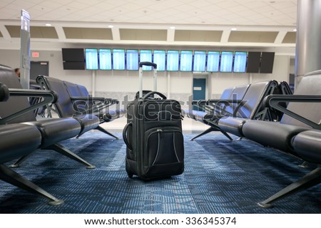 Black suitcase is standing in an airport departure/arrival hall as if lost or forgotten.