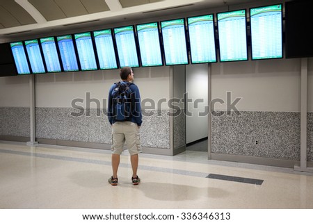 A young man is looking at an airport departure board.