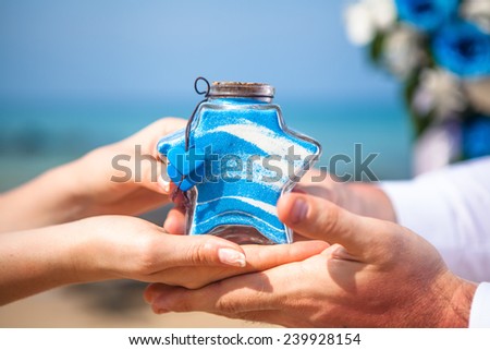 Male and female hands with a receptacle for sand ceremony on the background of the sea