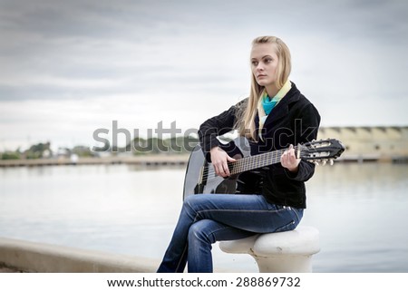 Beautiful blonde girl sitting on the bitt and playing the guitar