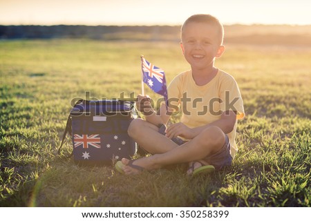 Cute smiling kid with flag of Australia sitting on the grass at sunset on Australia Day