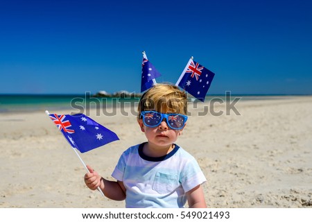 Cute smiling kid with Australian flags sitting on the sand at the beach on Australia Day