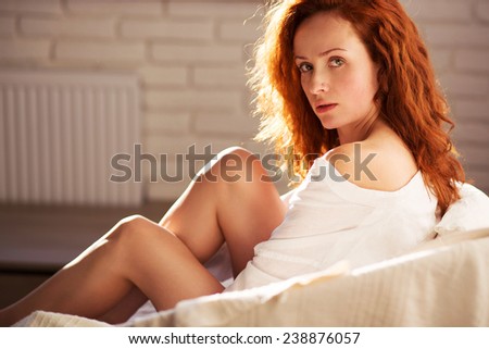 sexy red girl in the sunlight sitting in the chair with naked legs on the brick background