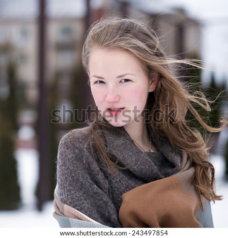 beautiful young girl in warm sweater and wrapping up with scarf on a windy day on school playground