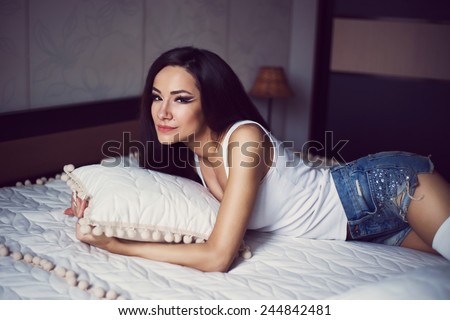 fashion model posing in the bed with bright make-up in stylish jeans shorts
