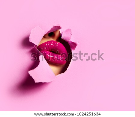 Beautiful plump bright lips of pink color peep into the slit of colored paper.