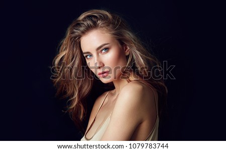 A beautiful tender girl in a silk top with beautiful long dark hair developing in the wind. Black background.