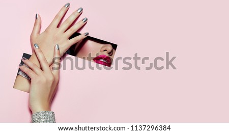 A girl with beautiful long fingers and silver nail polish with pink lipstick on the lips with metallic effect closes her eyes in a rectangular hole of pink paper of paper.