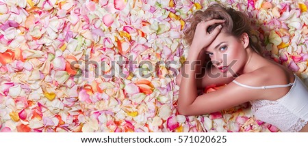 Valentine\'s Day. Loving girl. The girl in white dress lying on the floor in the petals of roses. Background of white, orange, red, pink rose petals. Pink lipstick on the lips from the beautiful girl.