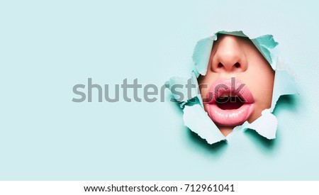 Beautiful plump bright lips of pink color peep into the slit of colored paper.make-up, makeup, advertising, facial, boutique, smooth skin, emotions, surprise.