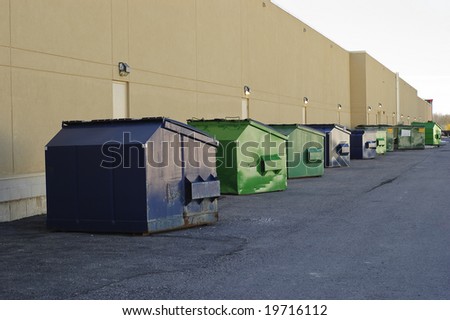 Blue and green industrial garbage bins lined up outside along commercial building