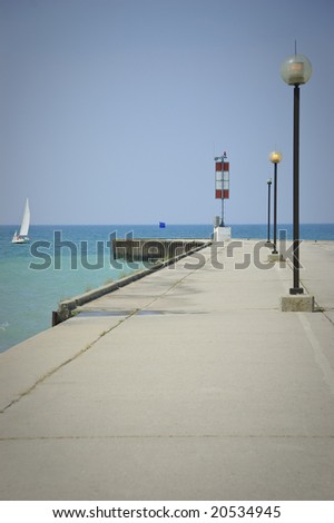 Concrete pier overlooking lake and sailboat under clear skies